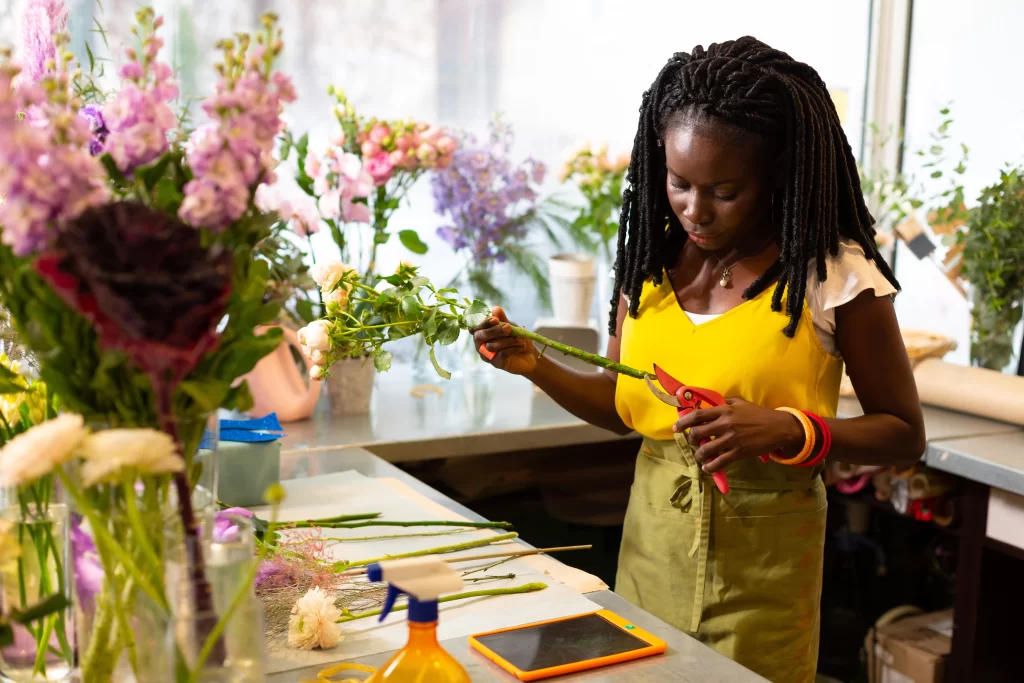 A young Black lady in a flower shop, cutting the tips of a flower 