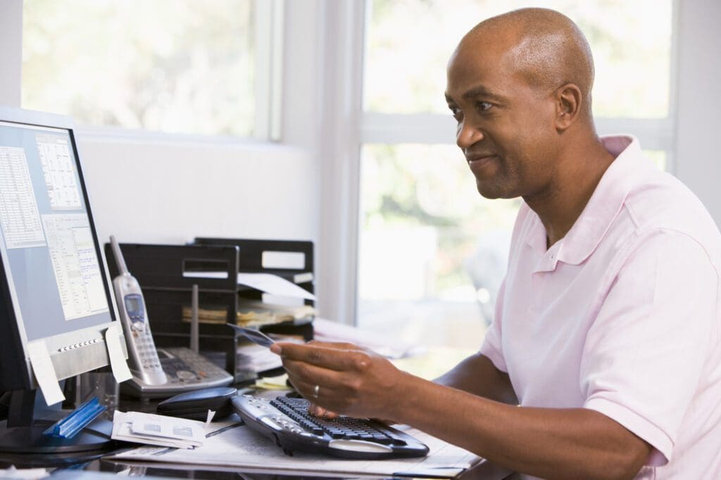 Man in home office using computer holding credit card and smiling