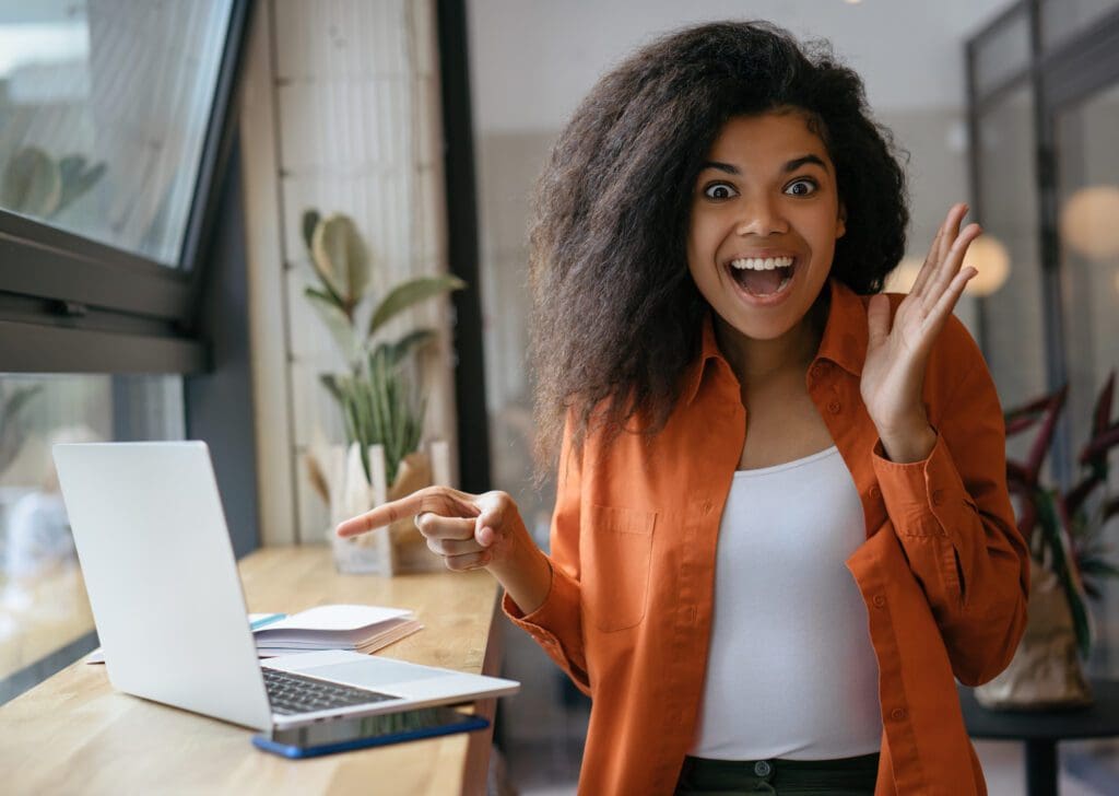 Excited African woman pointing finger on laptop
