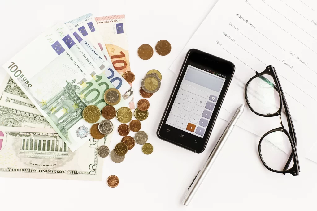 a photo of smart phone, money in coins and notes, eye glasses, a pen and a page of a notebook
