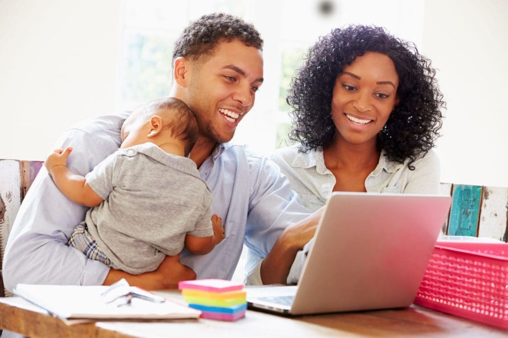 A young couple and a baby looking at a computer