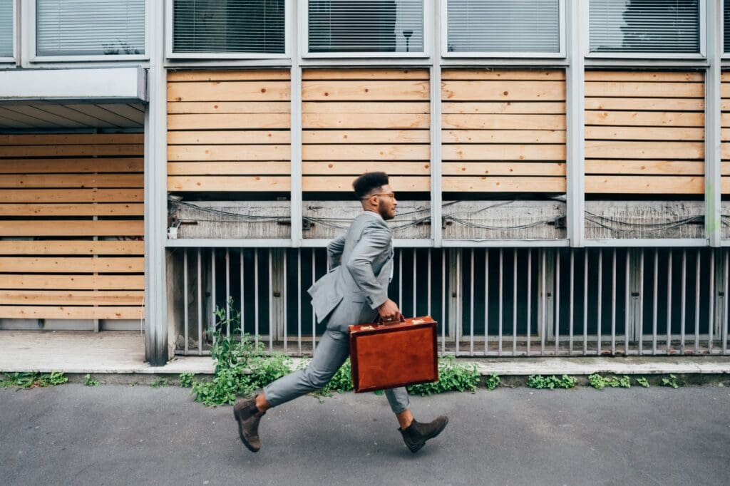 Young black businessman holding briefcase running late outdoor