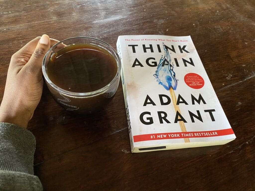 holding a cup of coffee with Think Again The Power of Knowing What You Don’t Know