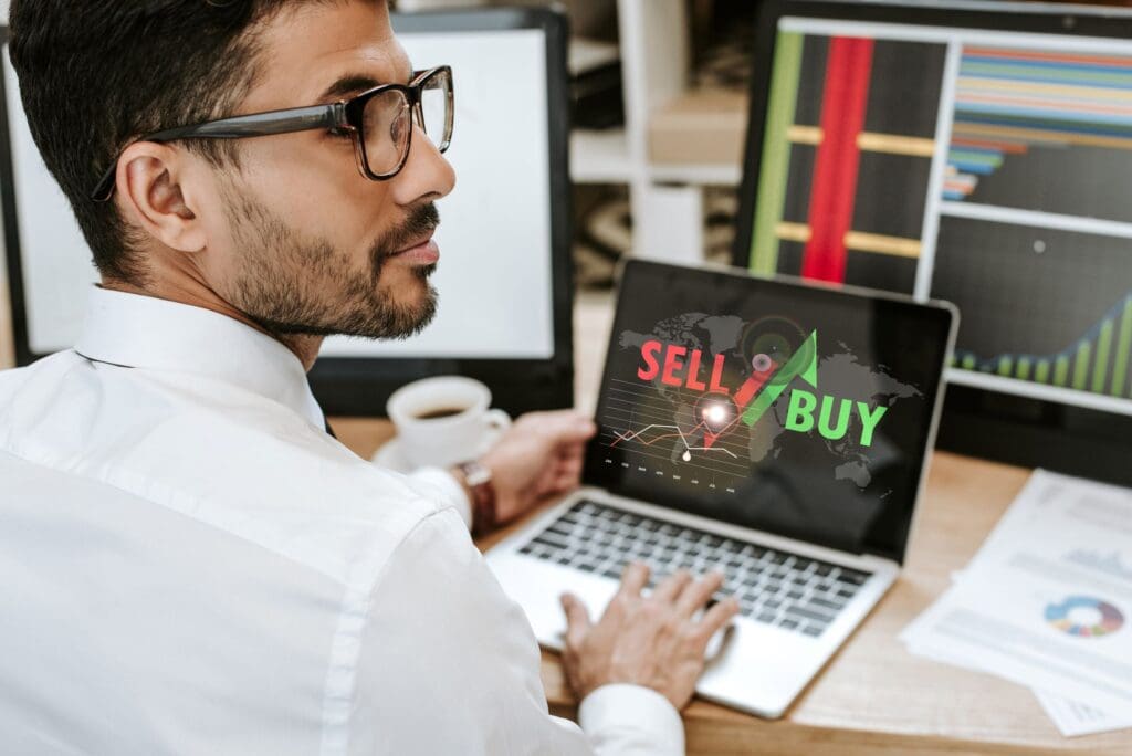 A young Arabic man trading on a laptop showing sell/buy option