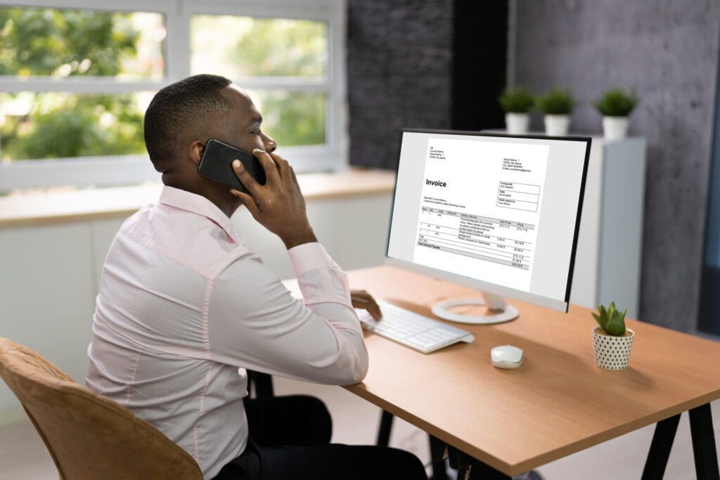 Young African man making a call while looking at an open desktop screen with an Invoice 