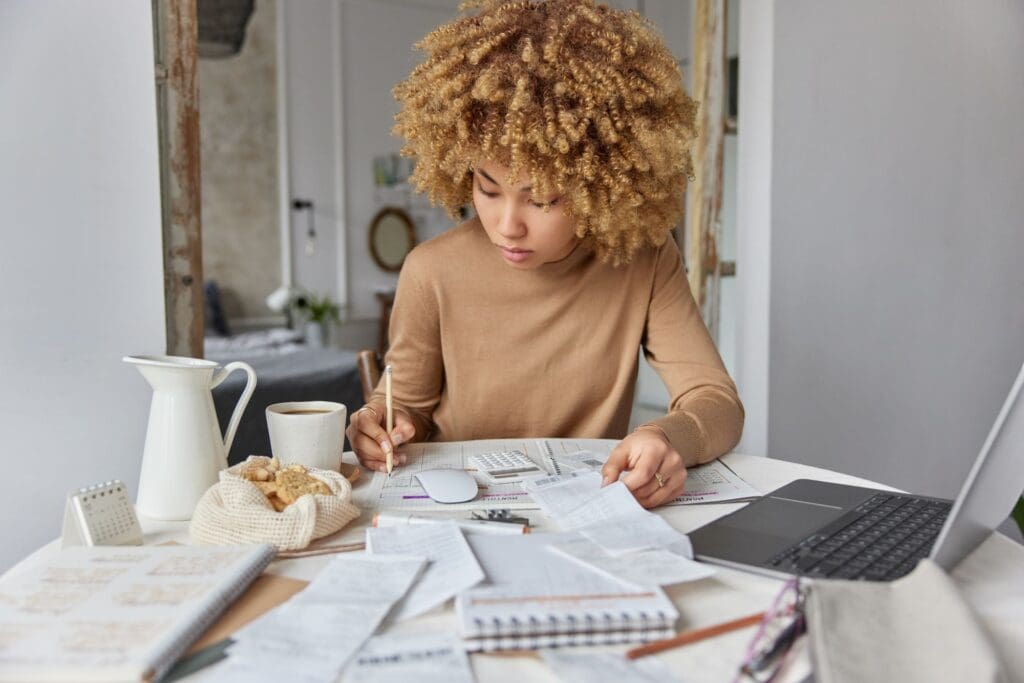 Curly haired woman sits at desk at home manages household budget studies financial bills