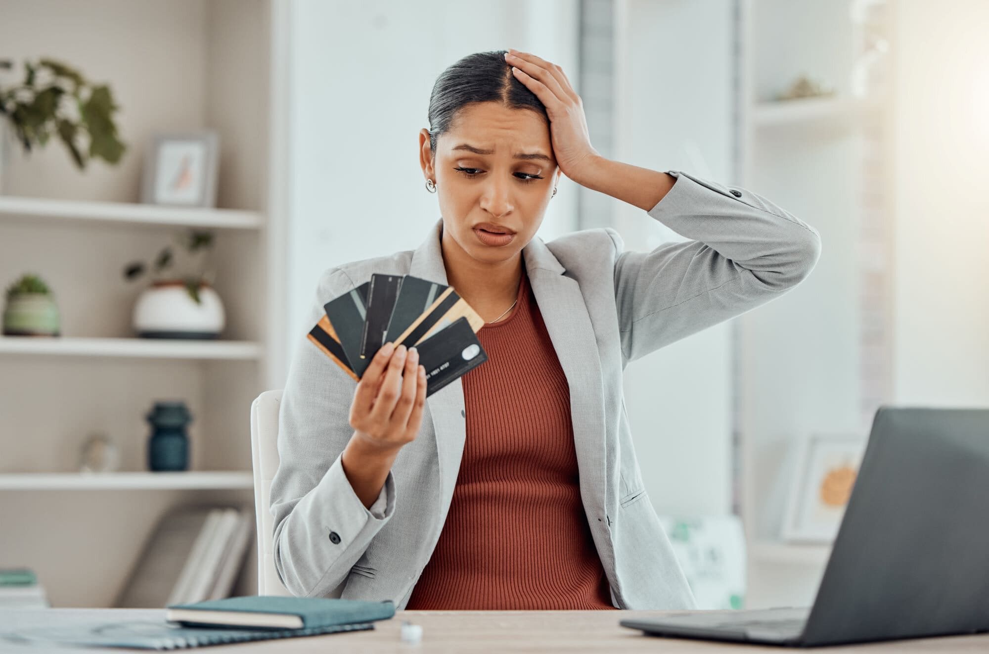 Financial stress, concerned and frustrated woman holding bank cards in her hand at her desk- good debt and bad debt