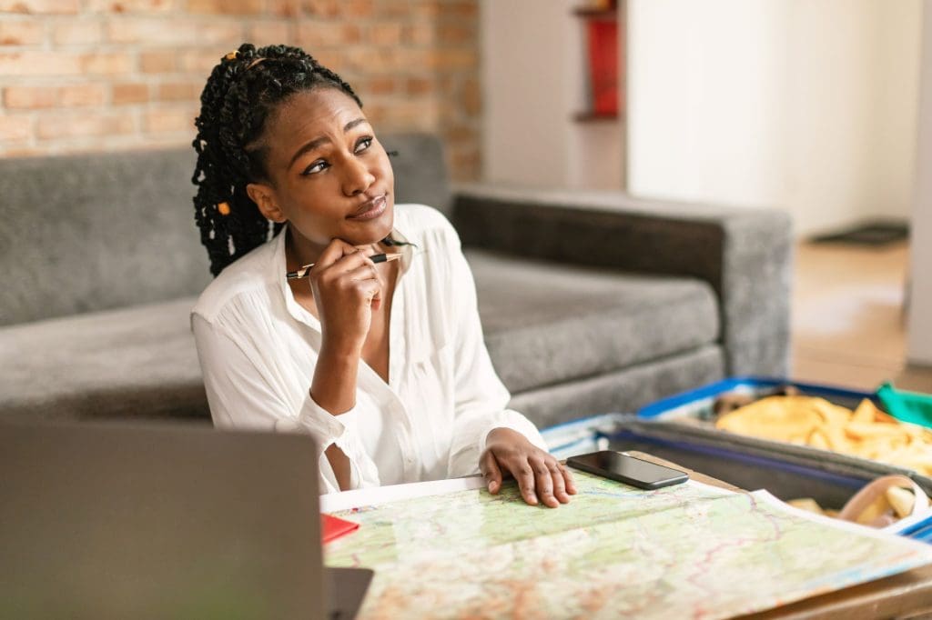 Dreamy african american woman planning future journey with map and laptop, thinking about traveling