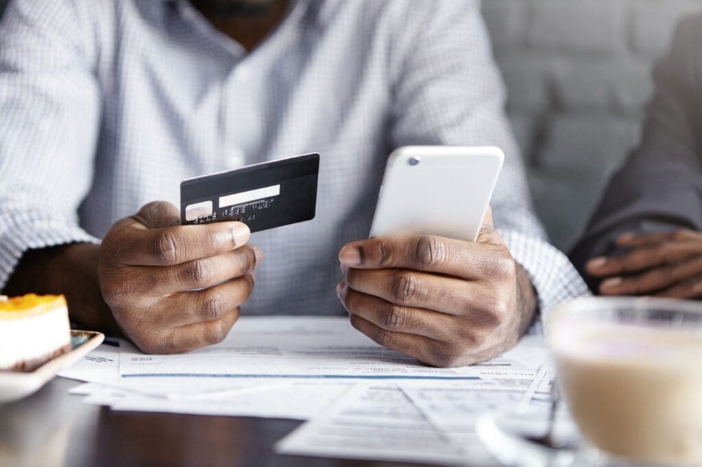 Young African Man Using Business Credit Card to Make Payment on Mobile Phone