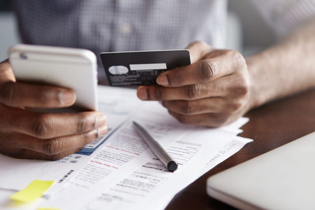 Cropped shot of African-American male holding cell phone in one and credit card in the other