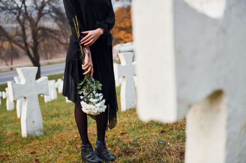 Young woman in black clothes visiting cemetery with many white crosses