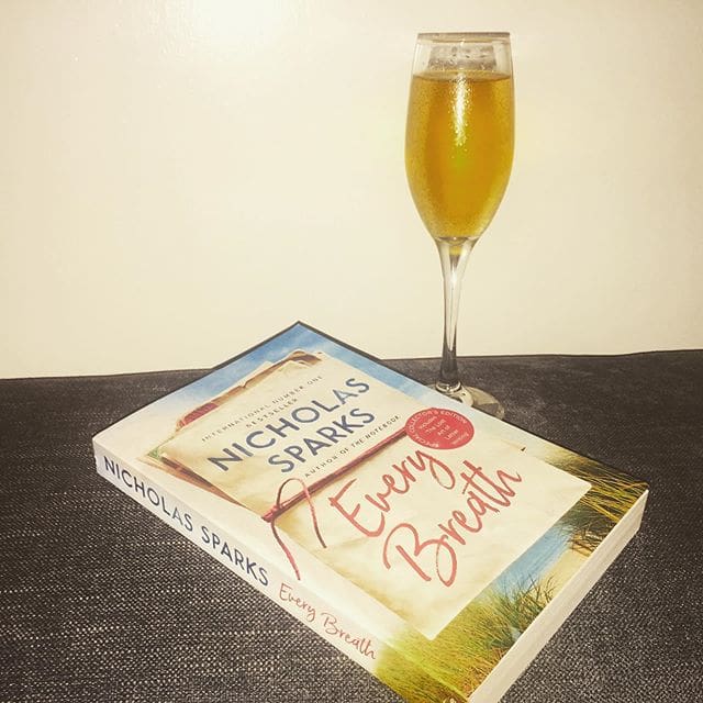 A book, Every Breath by Nicholas Sparks on the table with a wine glass