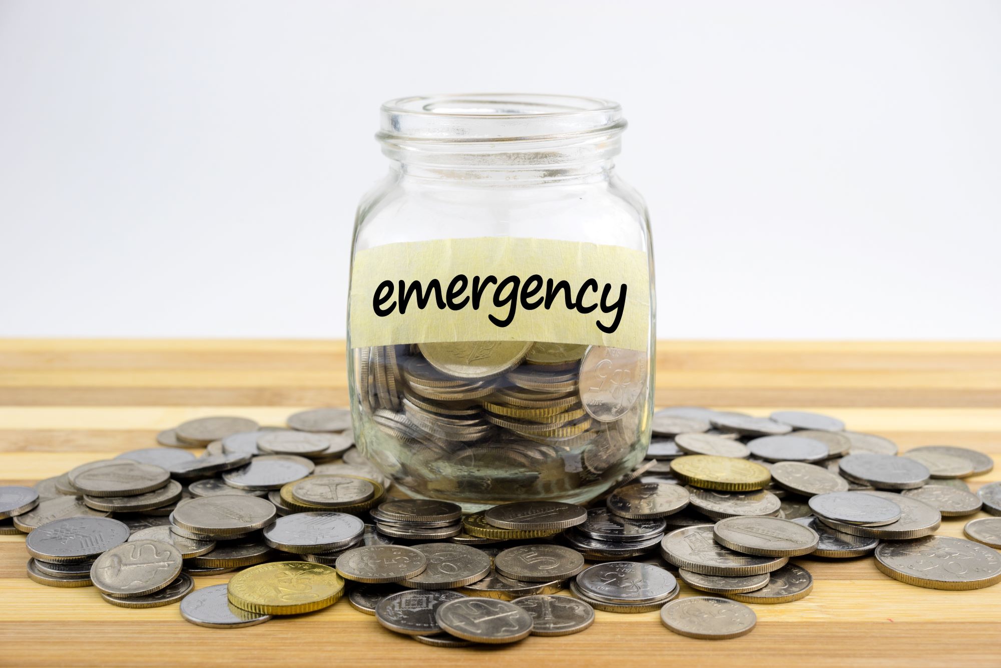 A glass jar on the table with coins and emergency label for emergency fund