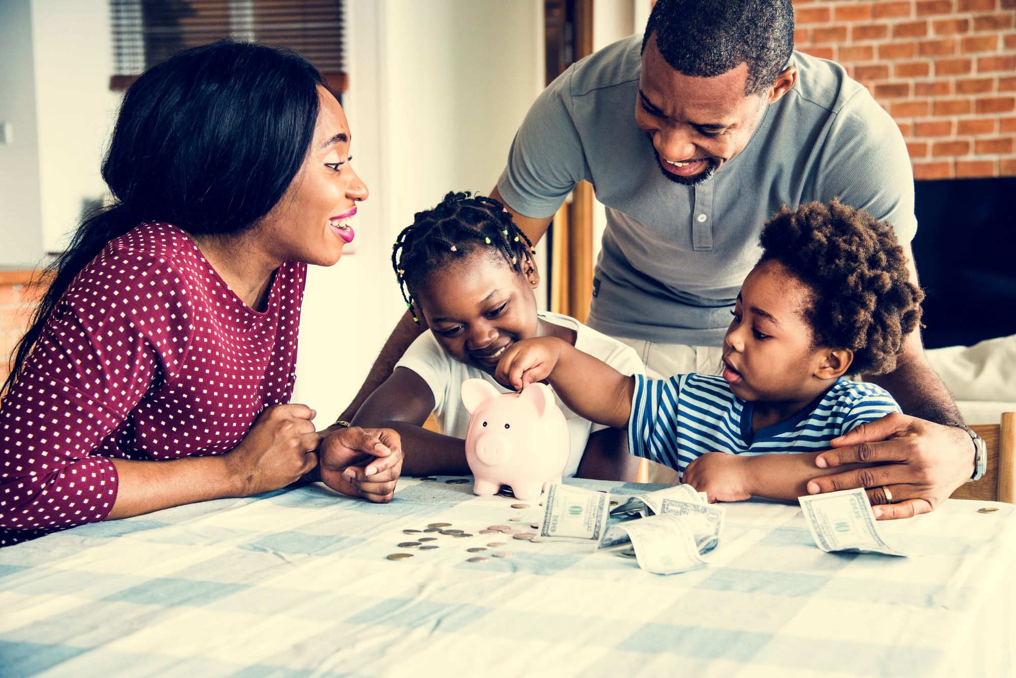 A young African family, dada, mom, and two children putting money in a piggy bank - saving for a SACCO