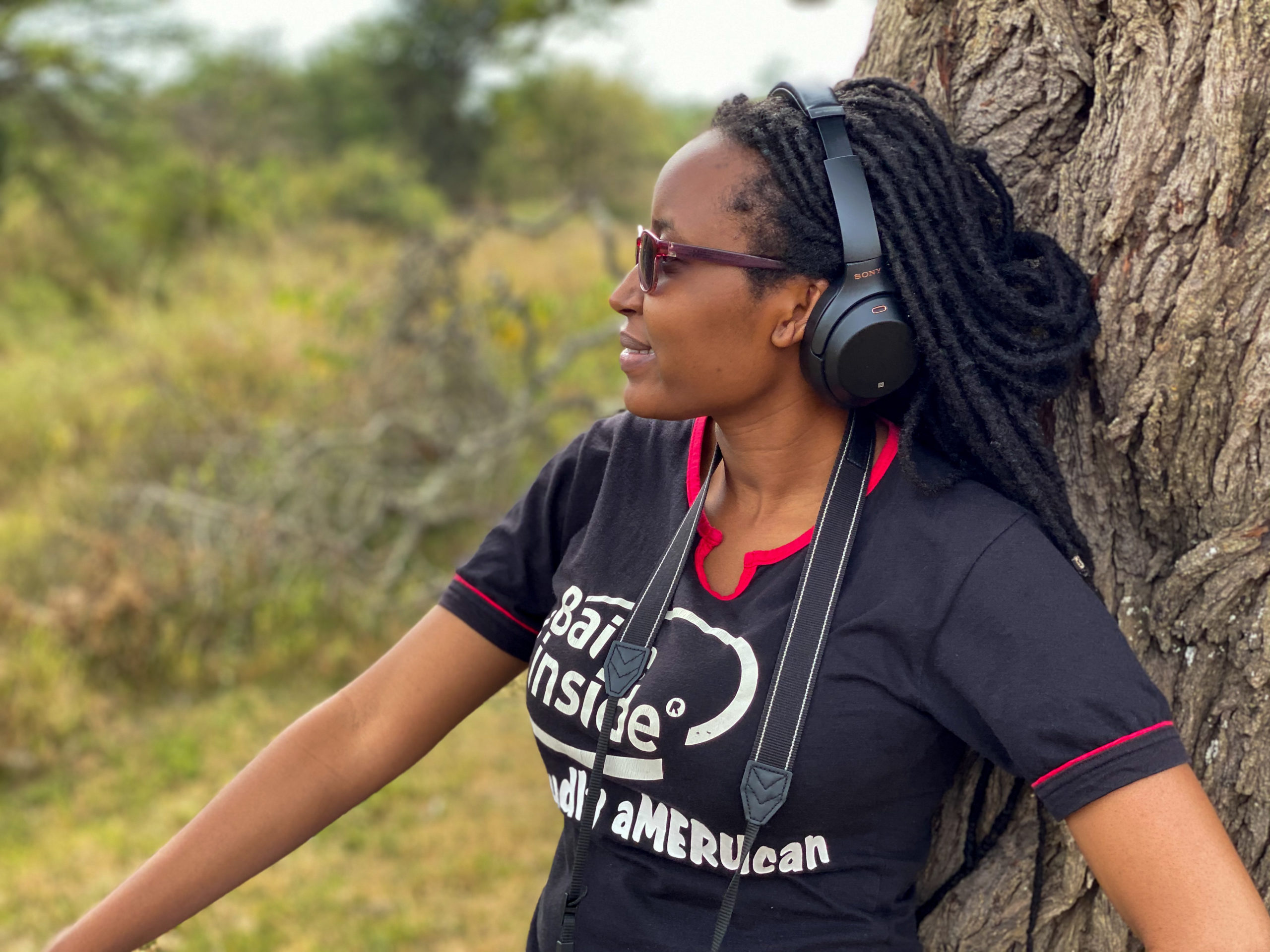 A young African lady leaning by a tree listening to music using noise cancelling headphones