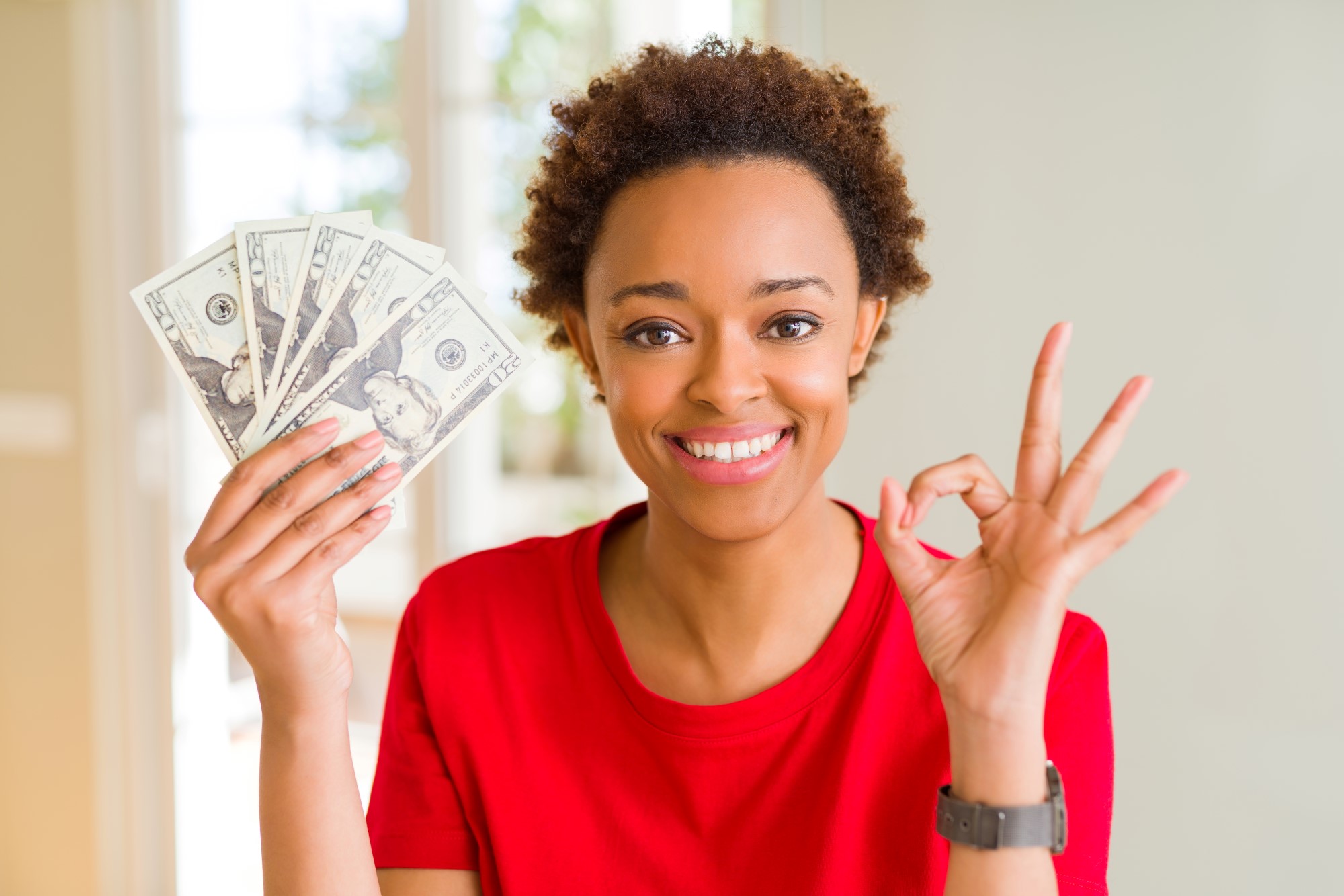 A young lady smiling and holding money (Financial Self-Care)