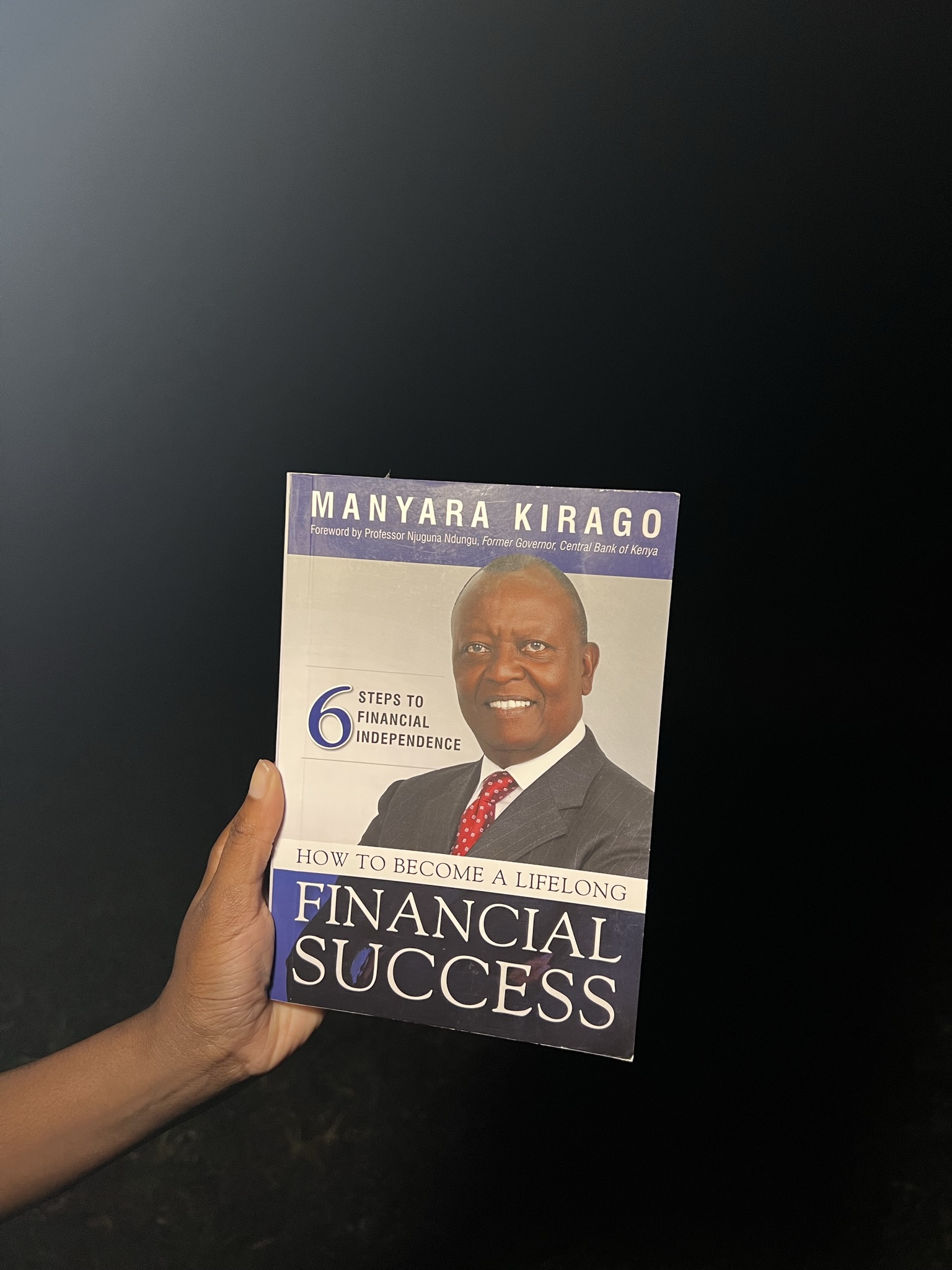 Holding a book, How to Become a Lifelong Financial Success by Manyara Kirago