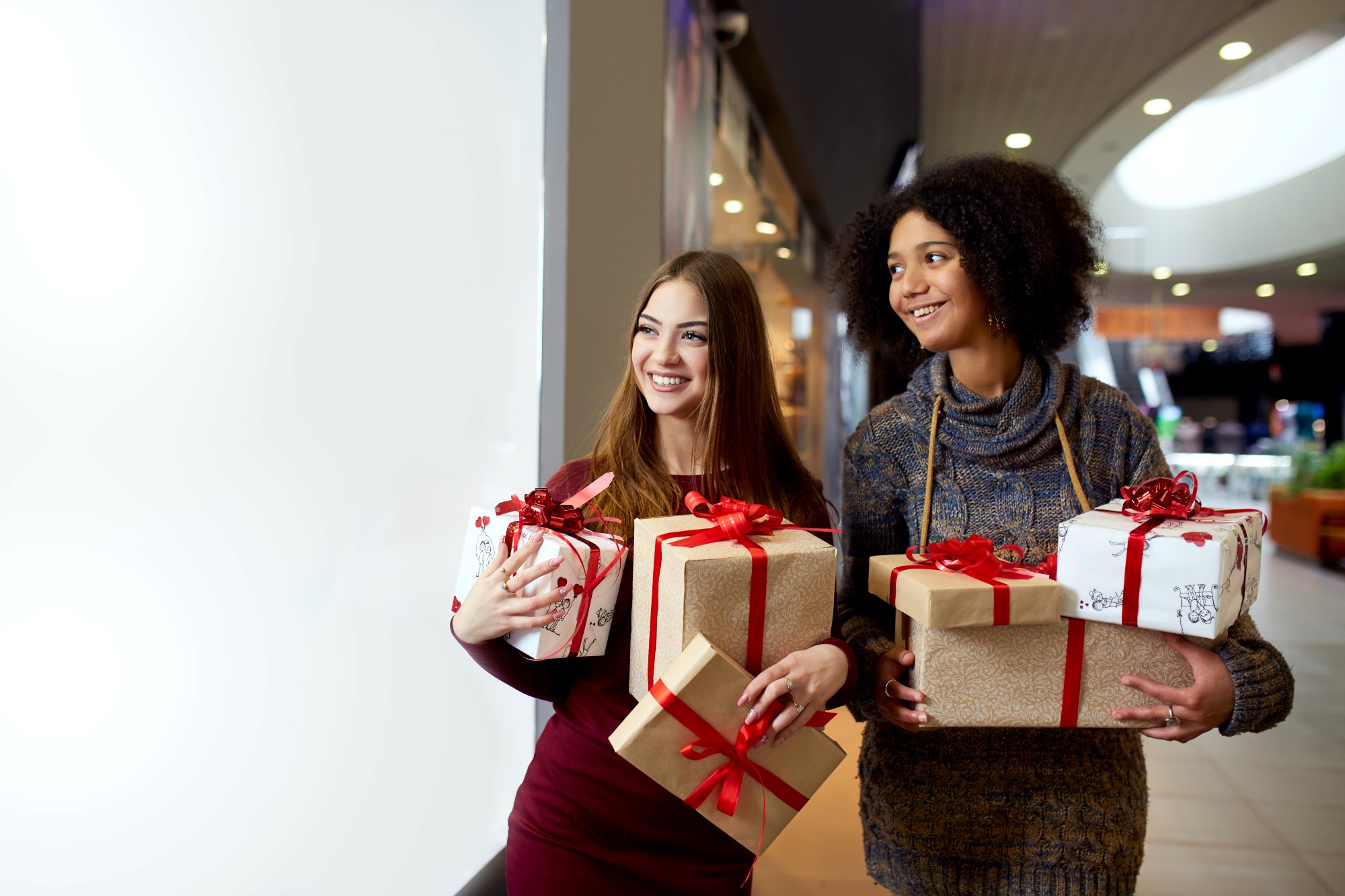 Two young ladies, White and African carrying holiday gifts at a Mall - manage money during the holiday season