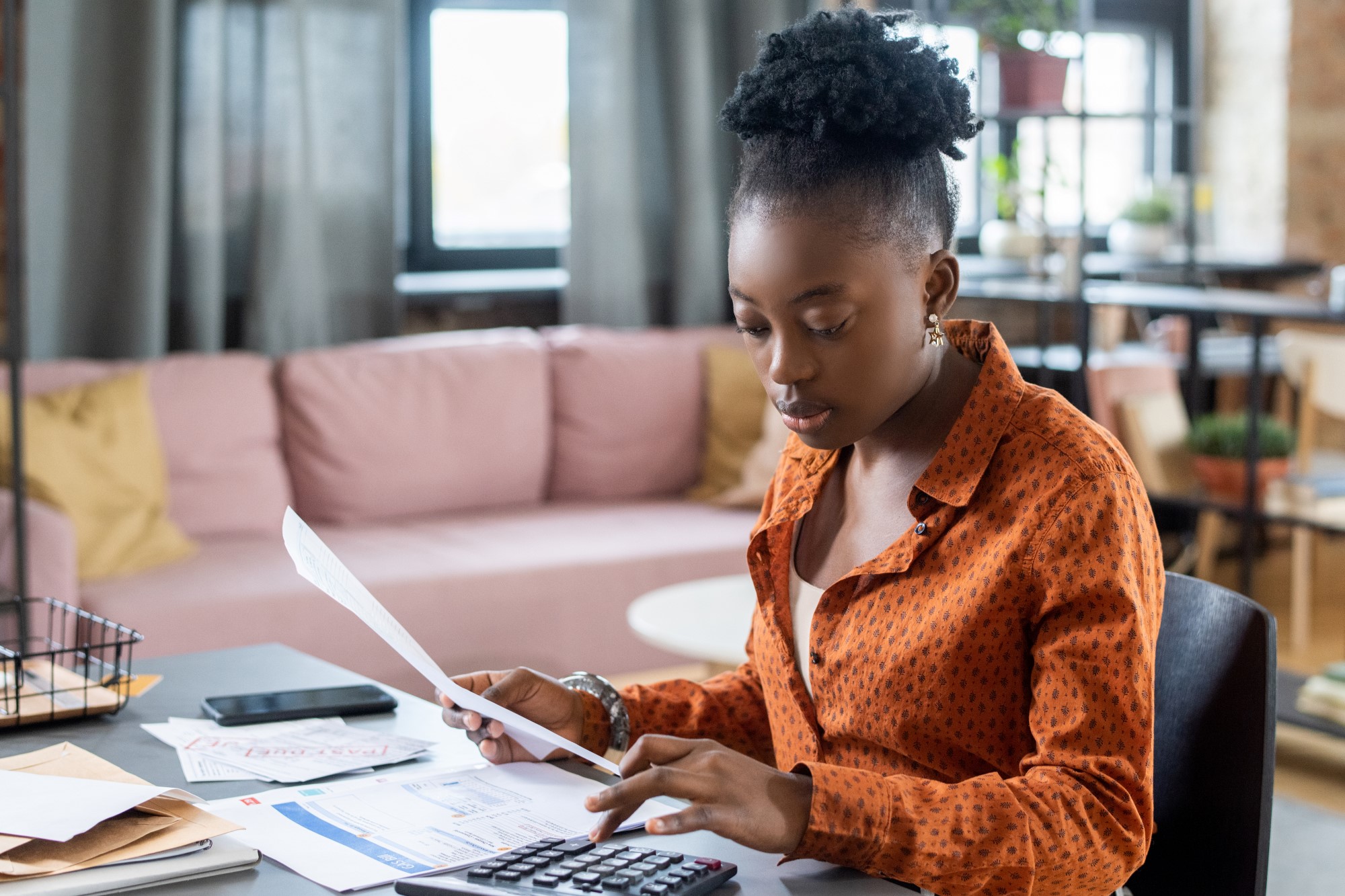 A young black lady sited on an office table, holding an invoice and doing calculations - tax guide for freelancers