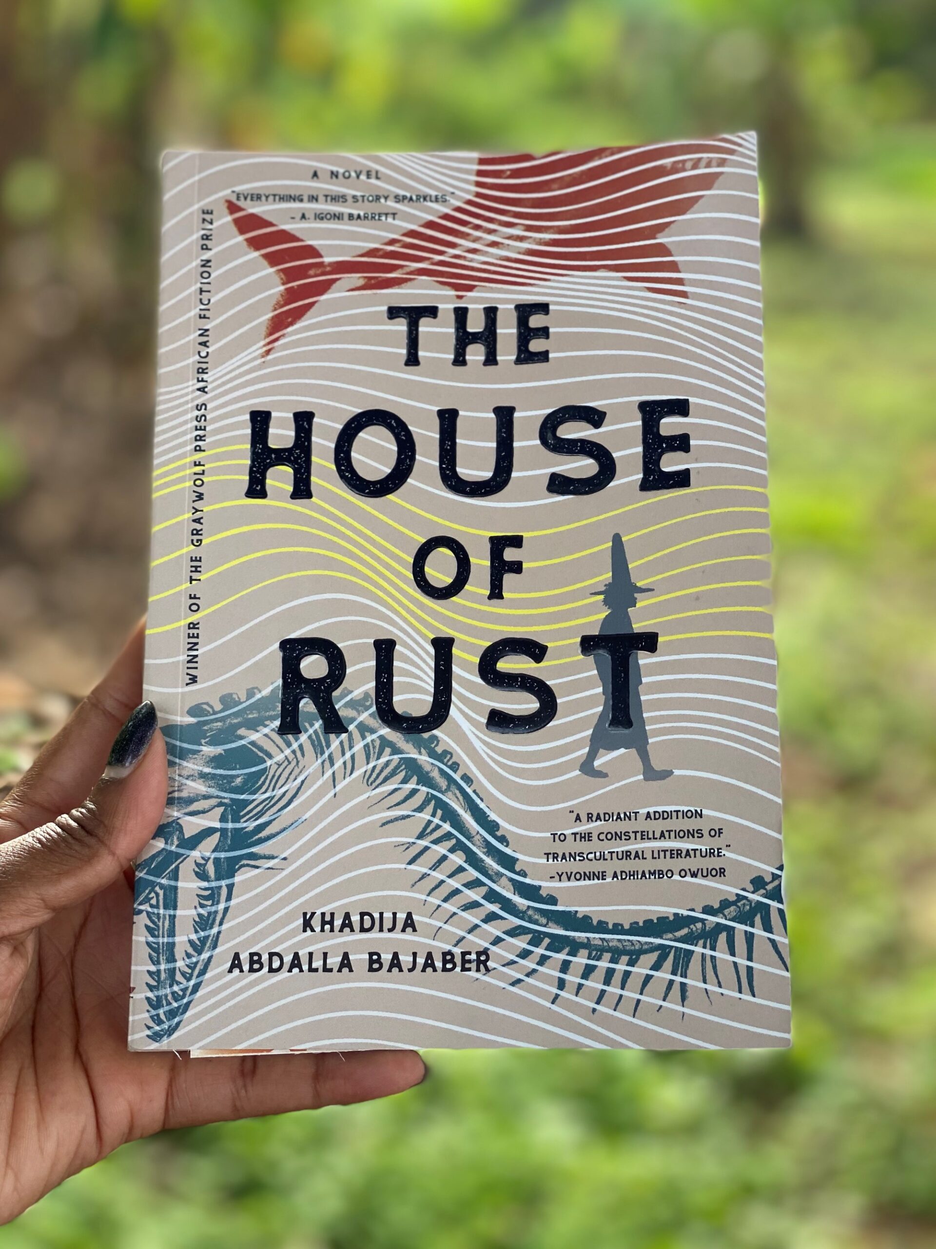 A Black lady's hand holding a copy of The House of Rust by Khadija Abdalla Bajaber