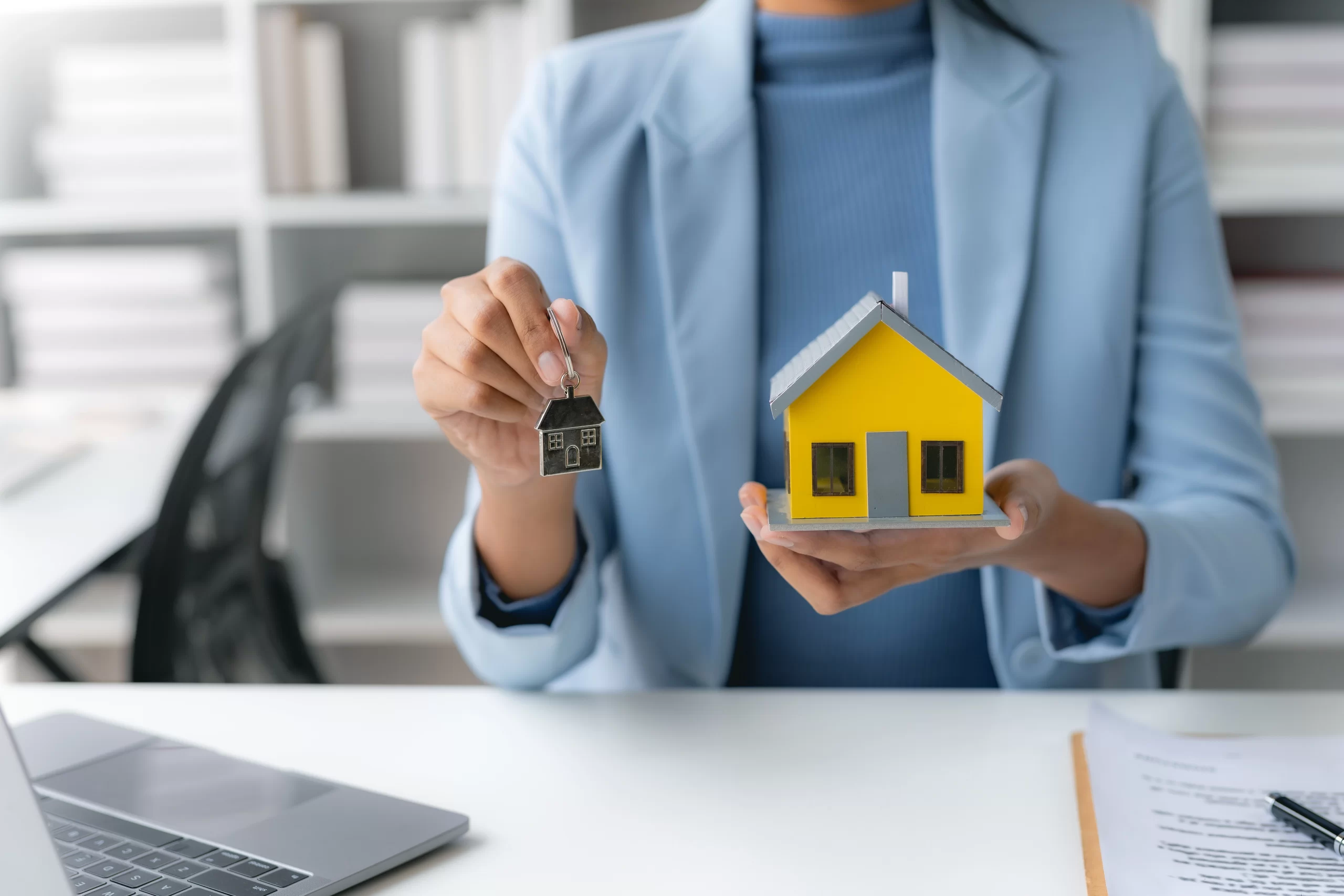female-employee- holding a yellow house model offering-domestic package-to-client-