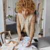 Indoor shot of curly haired woman stands near table full with papers invoices cheque and bills-Set Financial Boundaries
