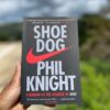 The hands of a young African woman holding a paperback copy of Shoe Dog by Phil Knight