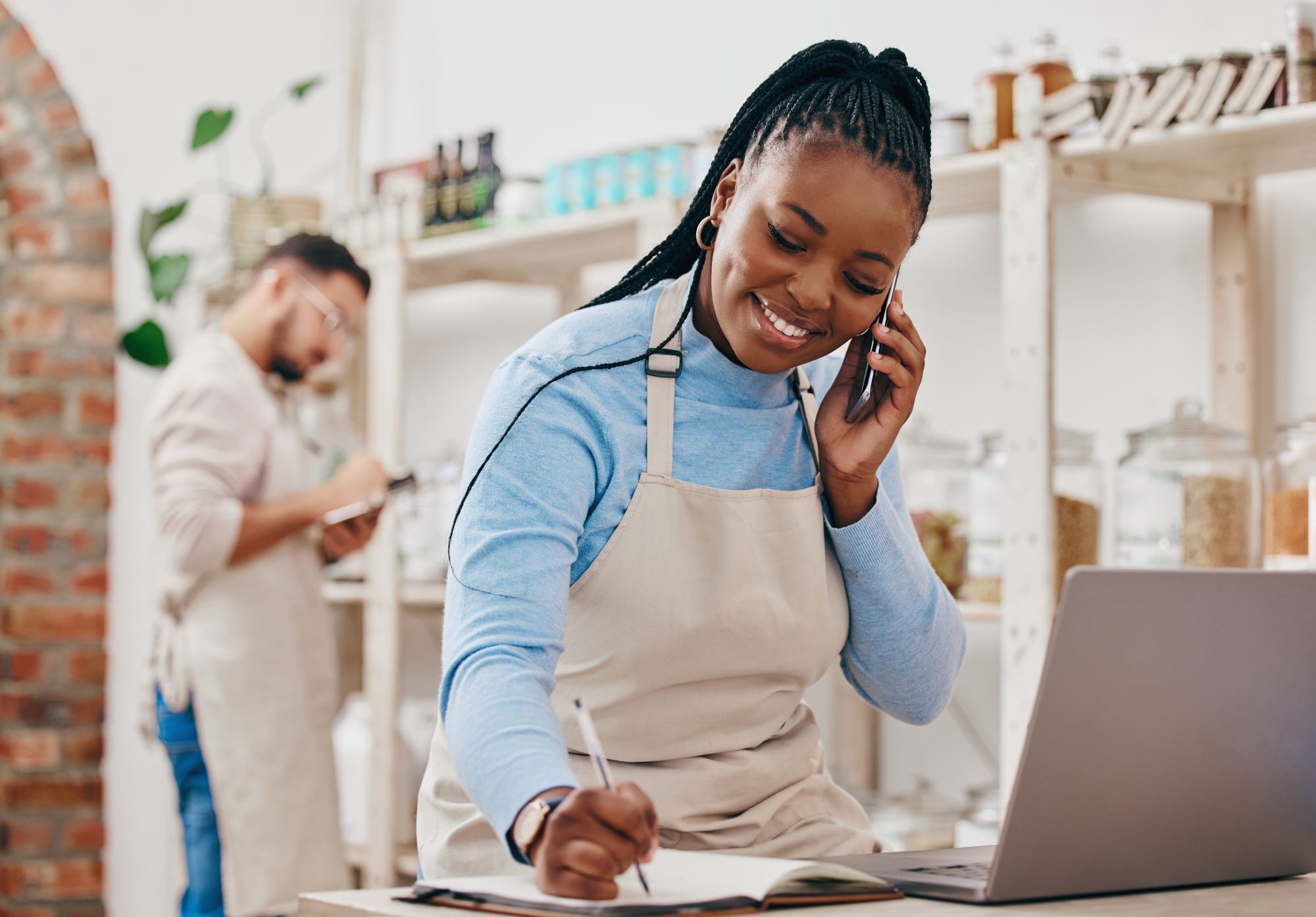 Black business woman taking cashier notes and making phone call with a white young colleague in the background-Tips to Get Paid Faster