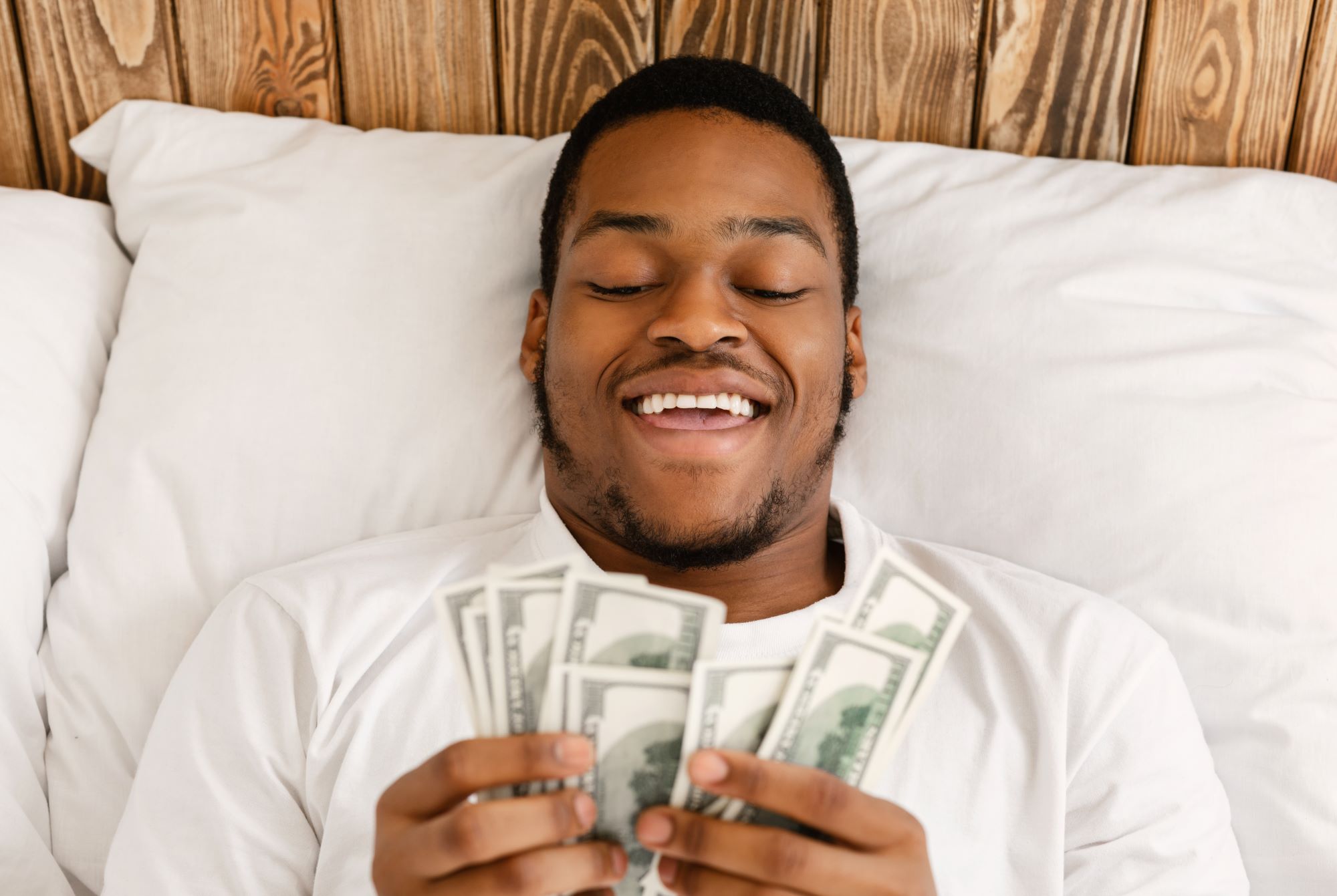 Happy African Man Holding Money Counting Cash Lying In Bed- enjoying returns from Fixed Income Funds