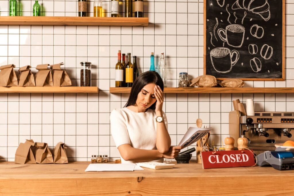Stressed cafe owner with closed eyes holding papers near table with calculator, card with closed sign