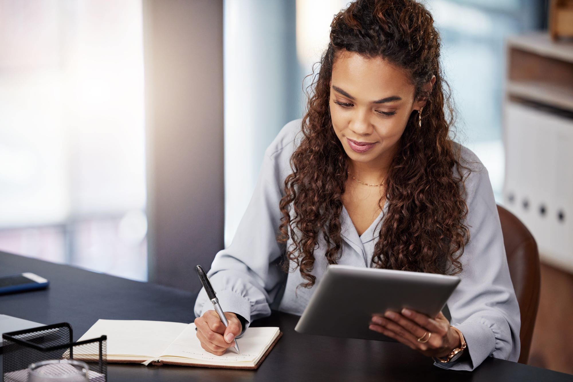 Young African woman writing in a notebook while holding tablet on the other hand- how to write a will in Kenya